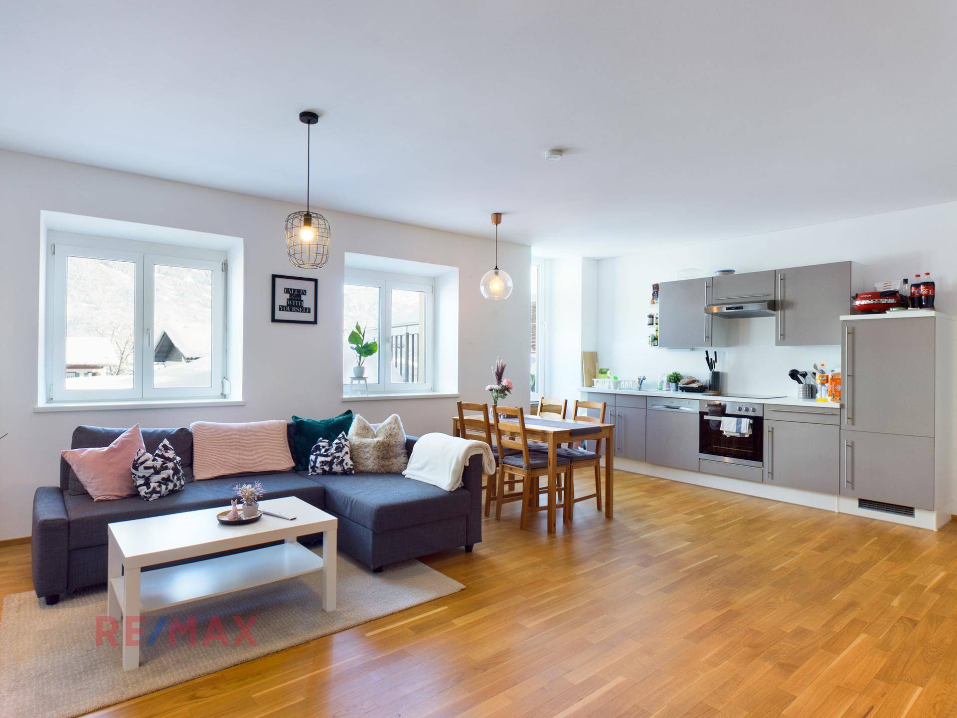 Heller offener Wohn-Essbereich mit moderner Küche, Sofa und Holzboden.