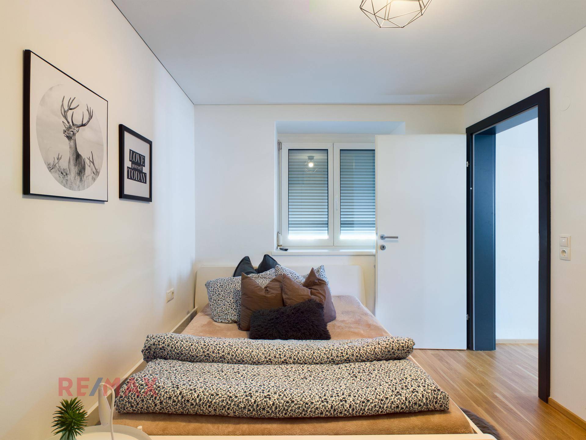 Helles Schlafzimmer mit Holzboden, Doppelbett und modernen Bildern an der Wand.
