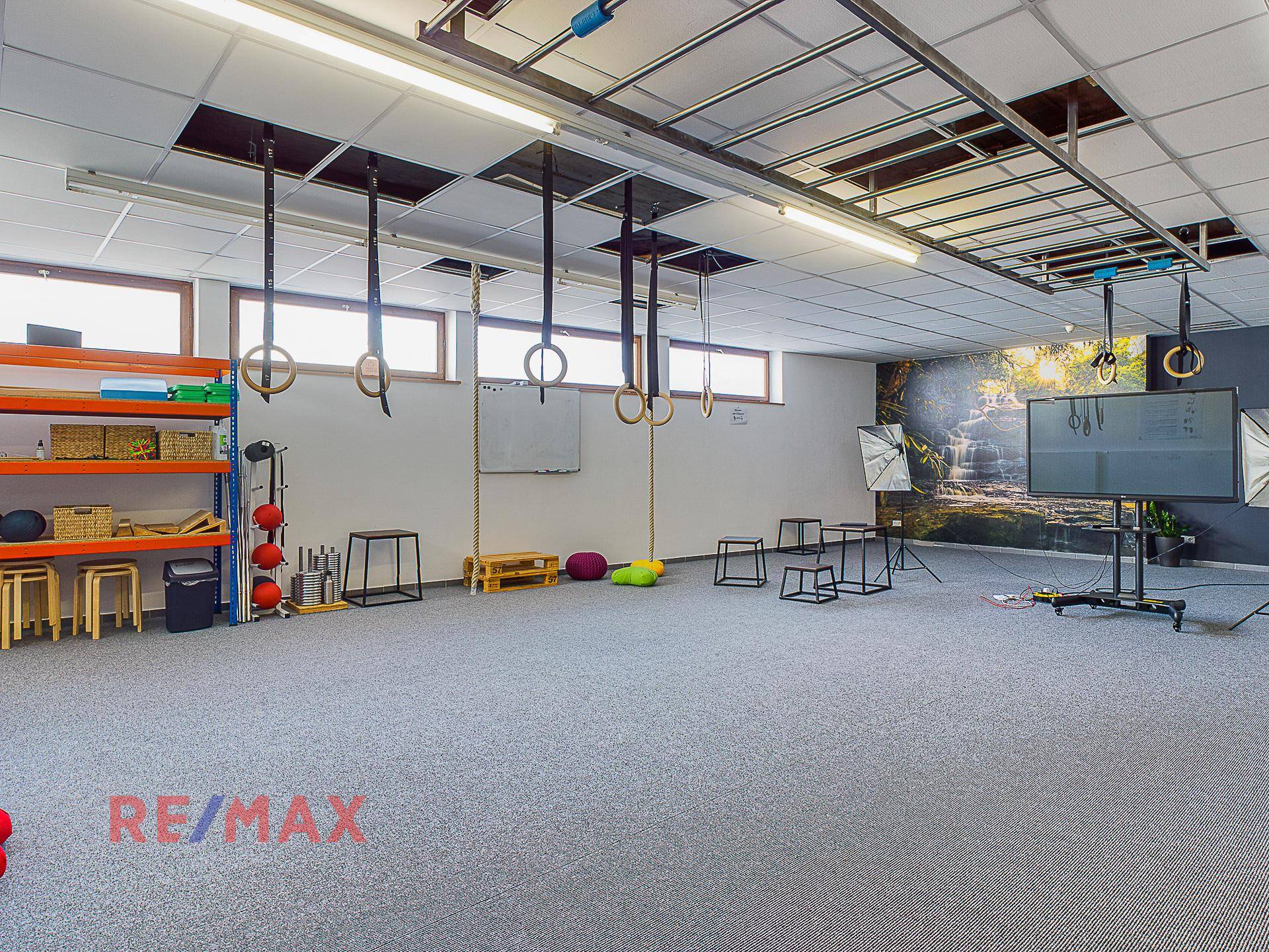 Geräumiger Sportraum mit Turnringen, Regalen und einem großen Bildschirm an der Wand.