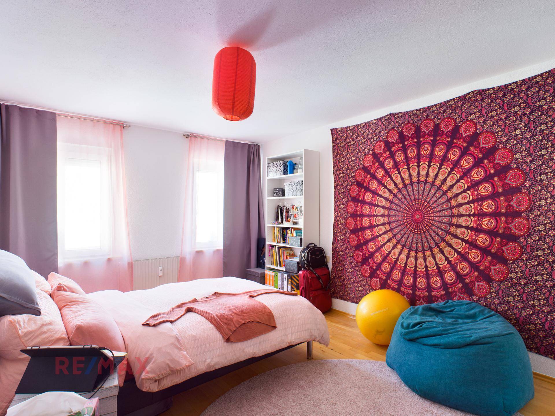 Farbenfrohes Schlafzimmer mit großem Wandteppich, Doppelbett und weichen Sitzsäcken.