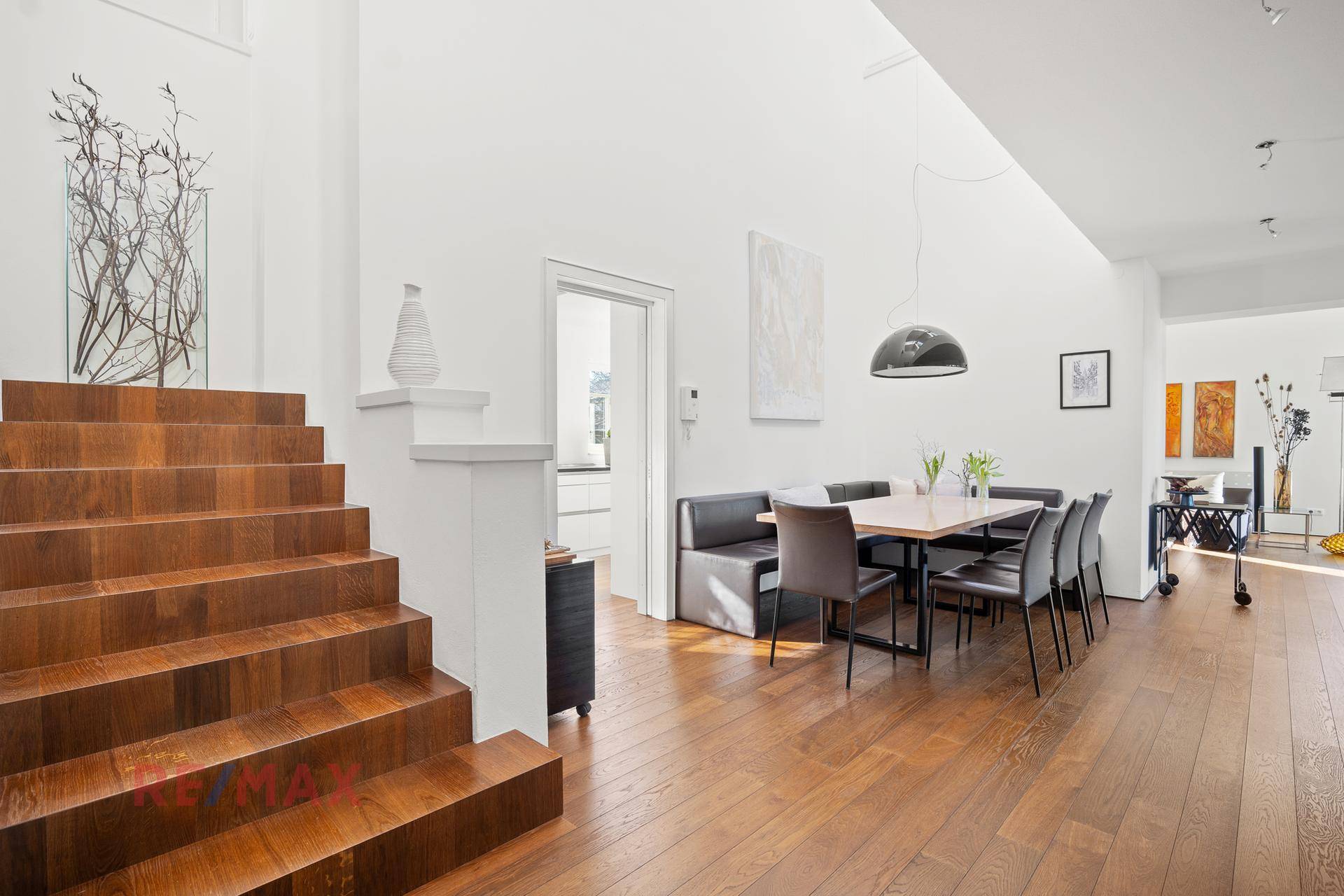 Offener Wohn- und Essbereich mit Holzboden, Holztreppe und modernem Esstisch.