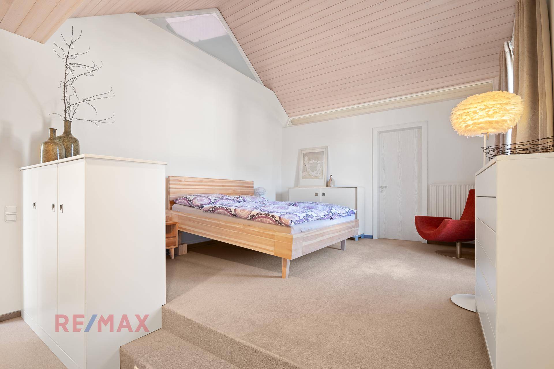 Helles Schlafzimmer mit Holzbett, Teppichboden und Holzdeckenverkleidung.