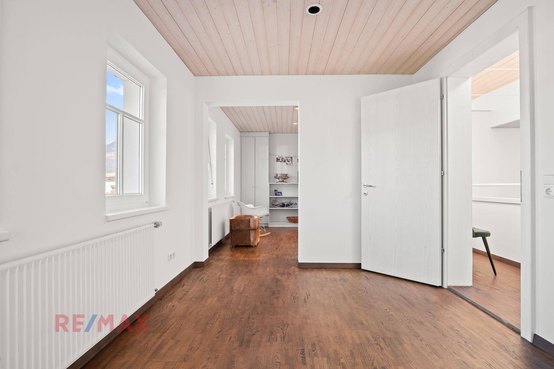 Geräumiger Raum mit Holzboden, Fenster und offener Verbindung zu anderen Zimmern.