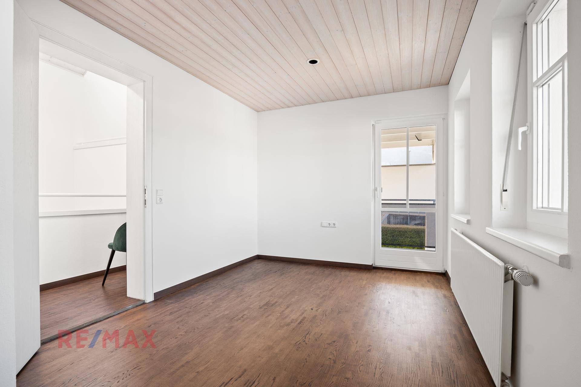 Heller Raum mit Holzboden, Fenster und Zugang zum Außenbereich oder Garten.
