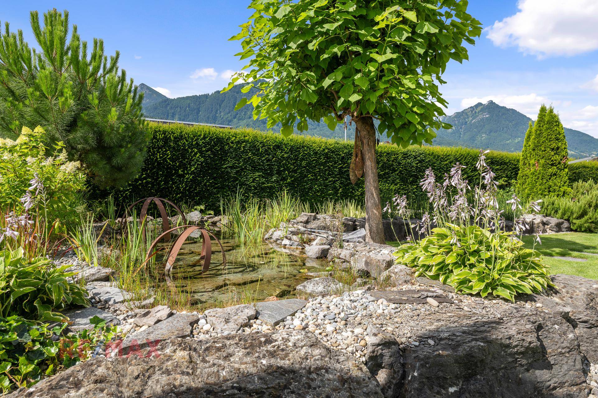 Detailansicht des Gartens mit kleinem Teich, Felsen und vielfältiger Bepflanzung.
