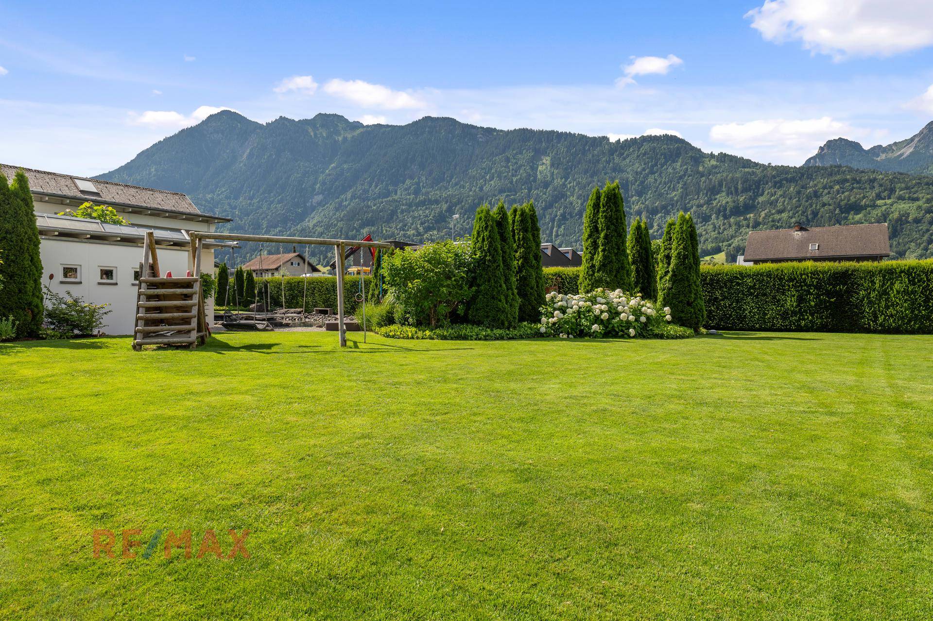 Großer Garten mit Rasenfläche, Schaukel und Blick auf die umliegende Berglandschaft.