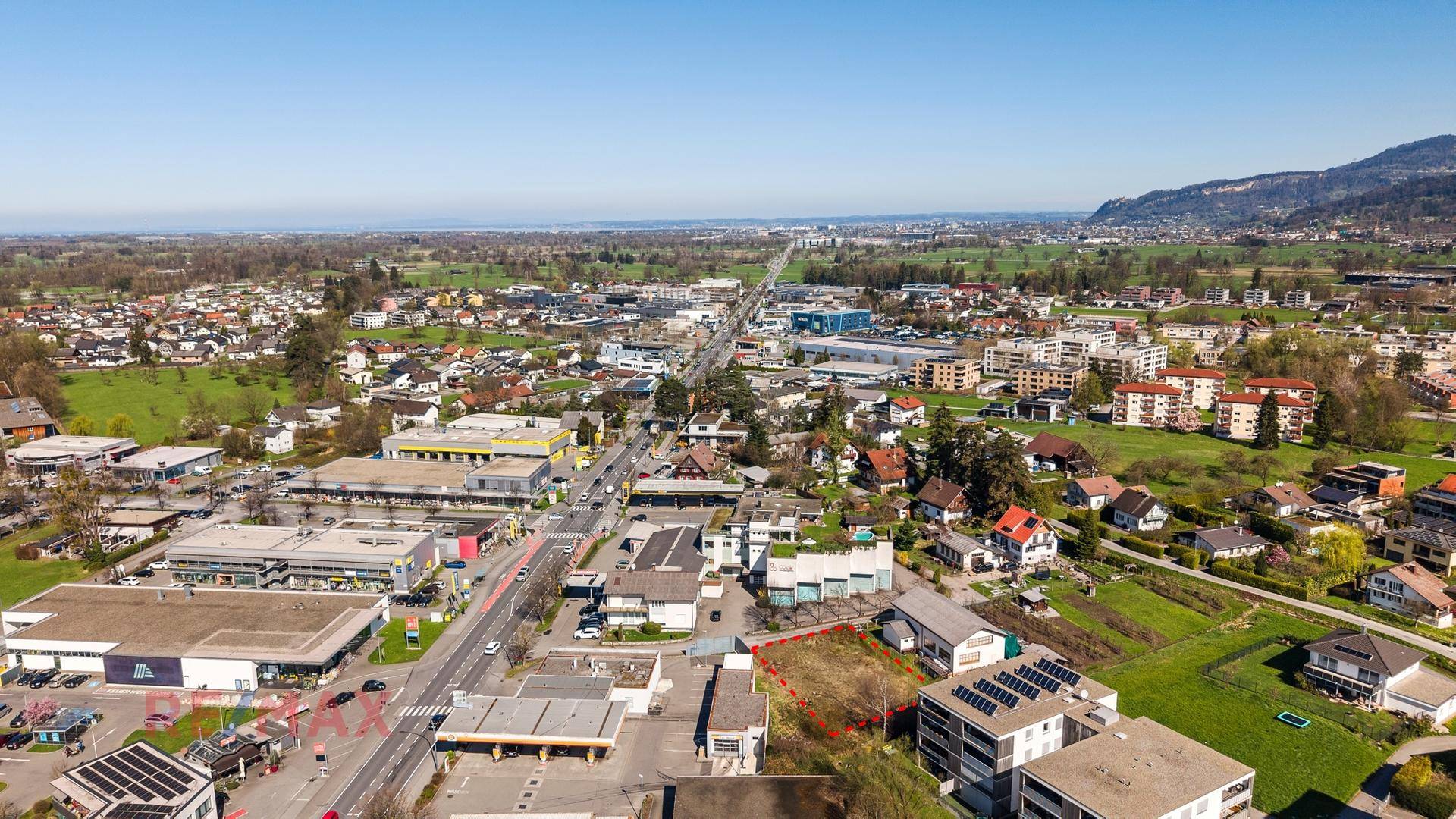 Luftaufnahme des Grundstücks im Kontext einer Vorstadtlandschaft mit Hauptstraße und Bergen in der Ferne.