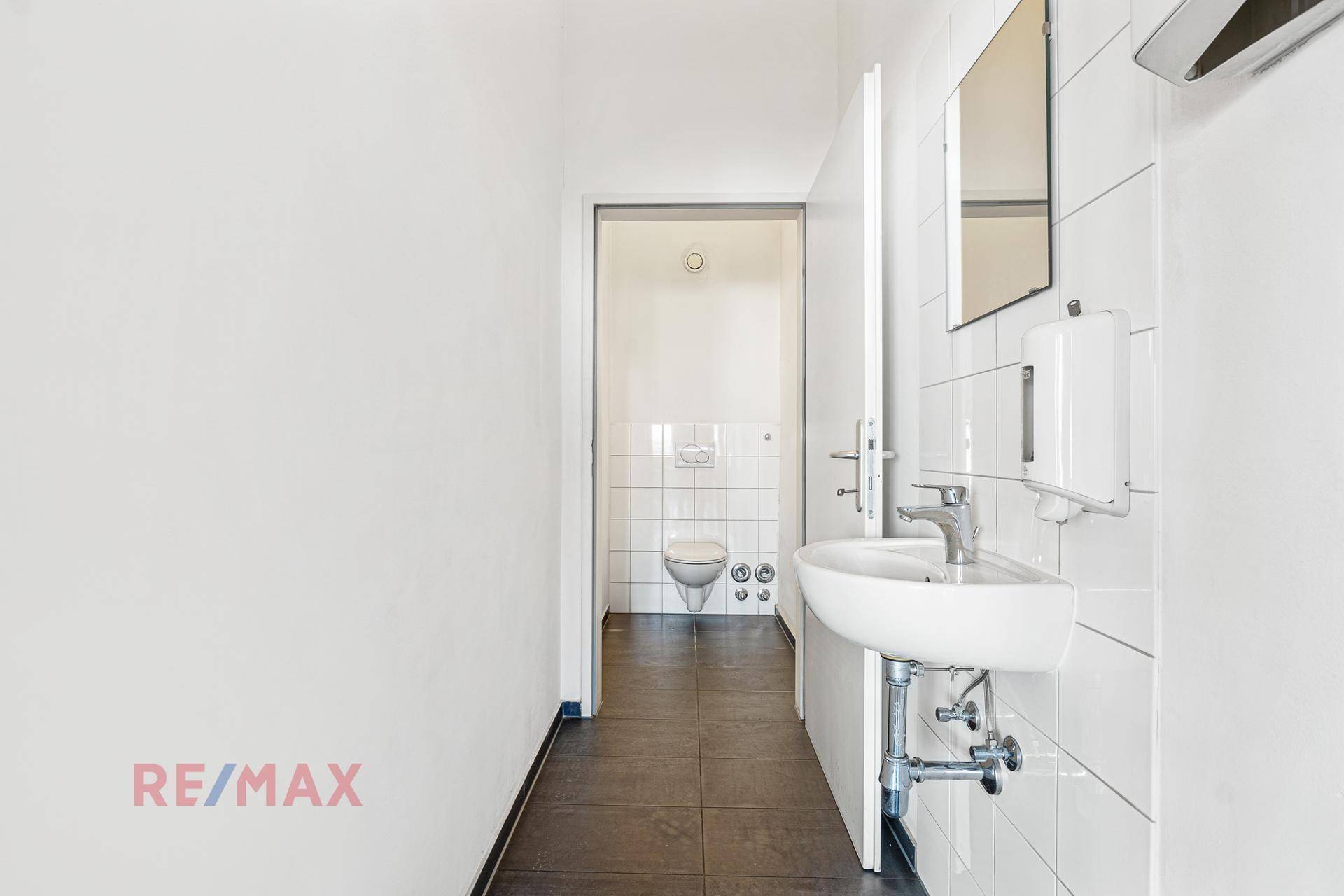 Schmaler Flur führt zu einer Toilette mit Waschbecken und weißen Fliesen an den Wänden.