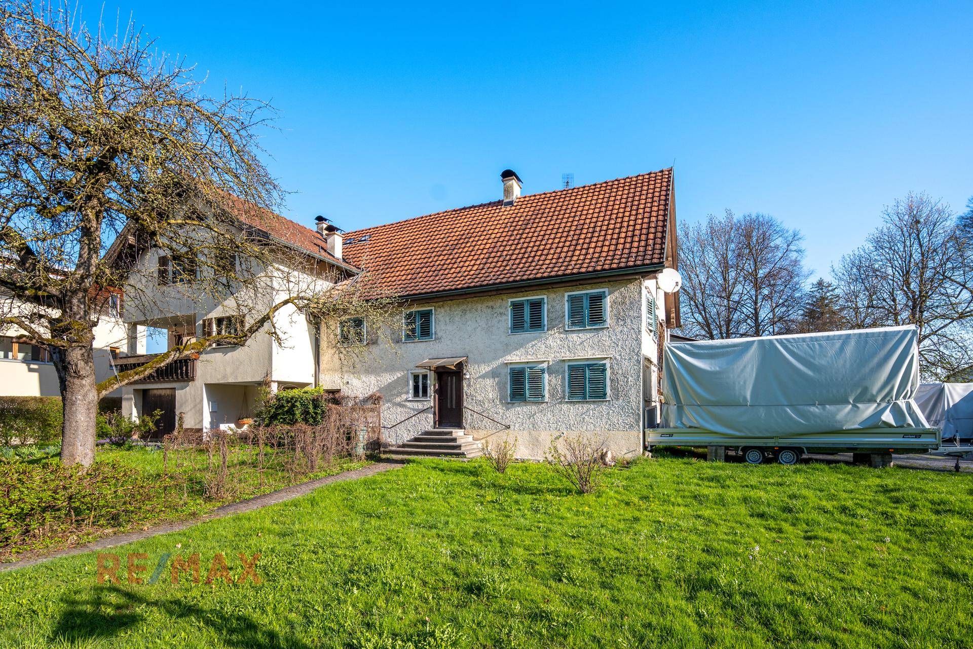 Ansicht des Wohnhauses von vorne mit grüner Rasenfläche und traditionellen Fensterläden.