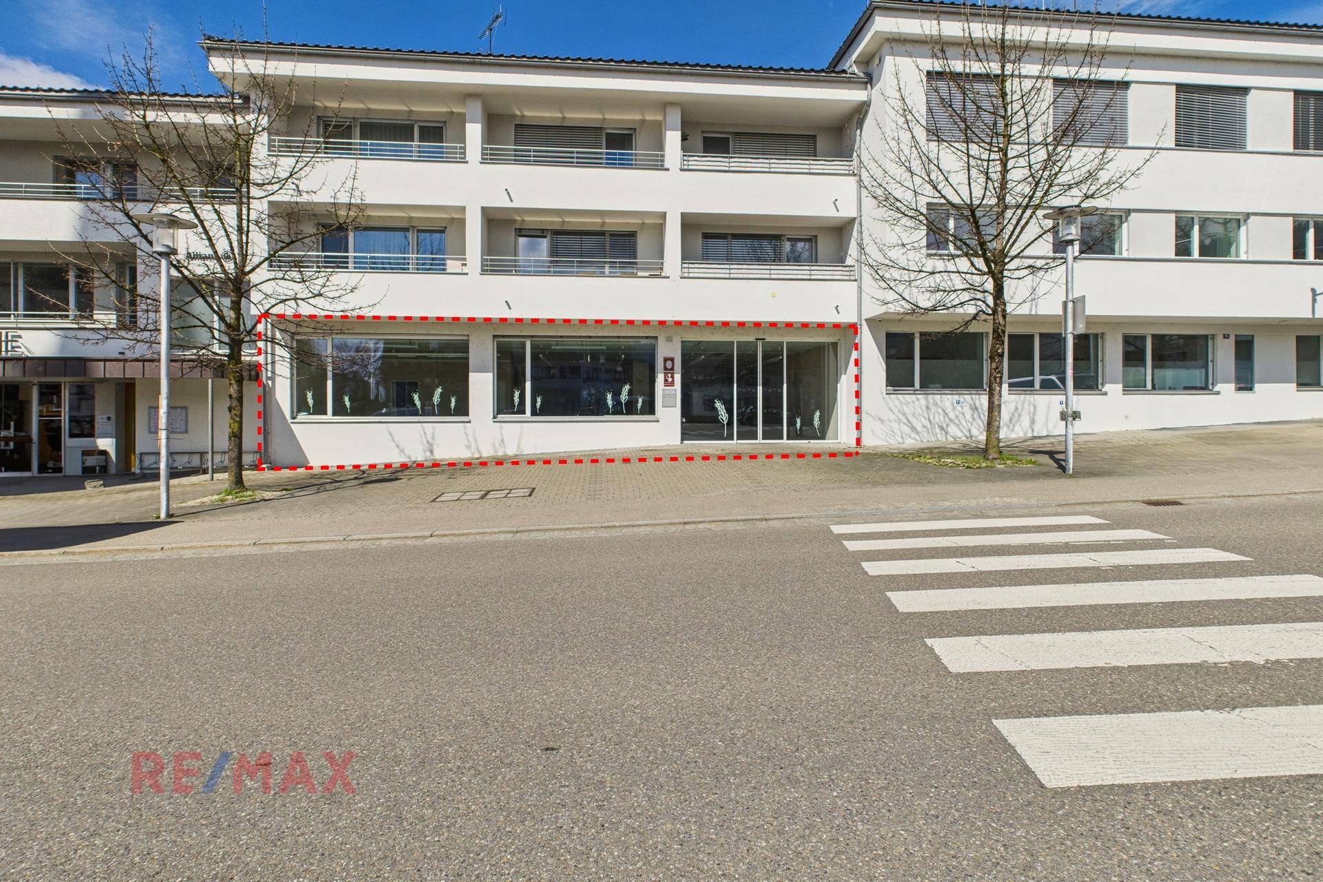 Ansicht des Geschäftsgebäudes von der Straße aus, mit breiten Schaufenstern und einem Zebrastreifen davor.