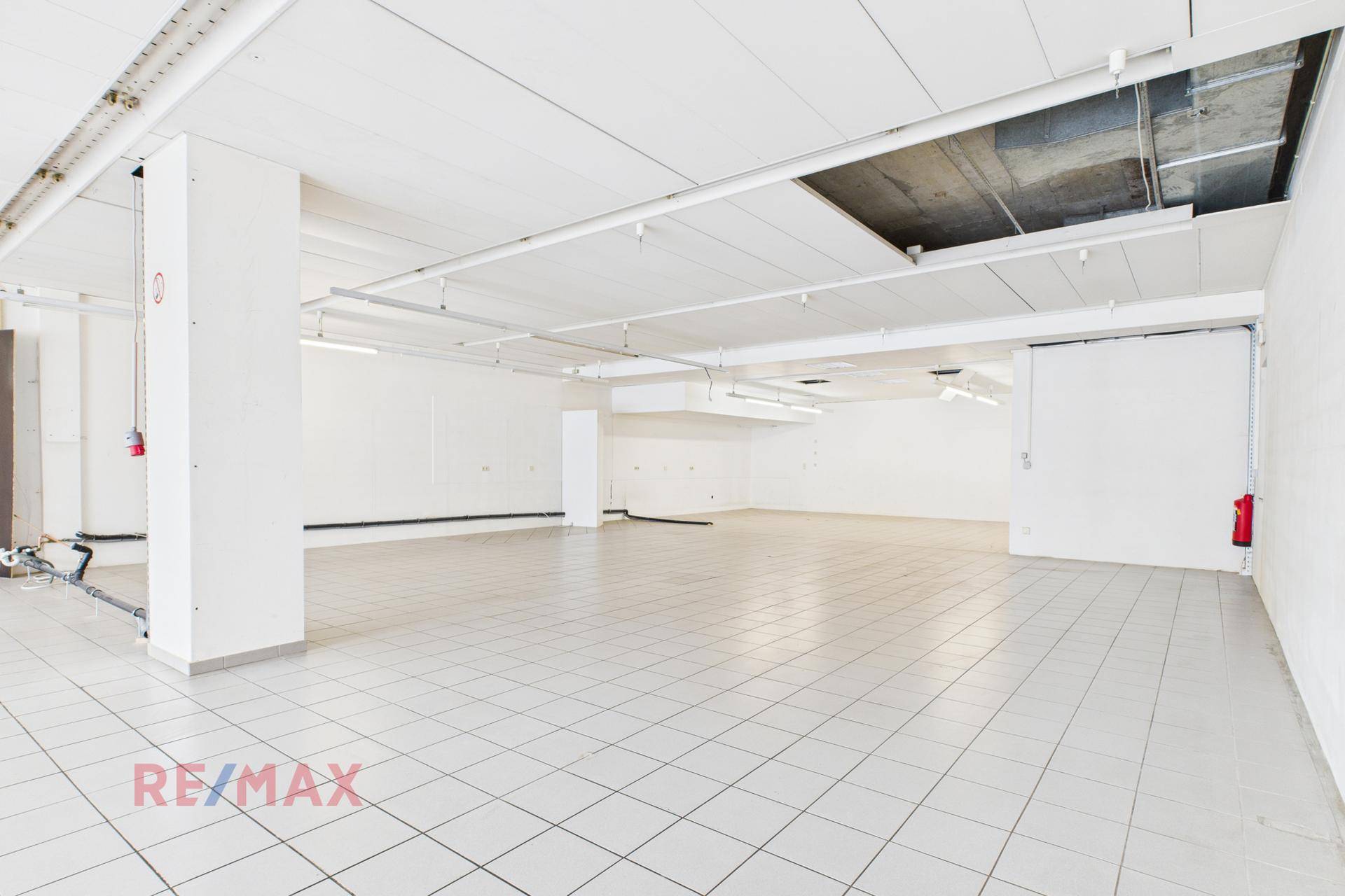 Weitläufiger Verkaufsraum mit weißen Fliesen und sichtbaren Installationen an der Decke.