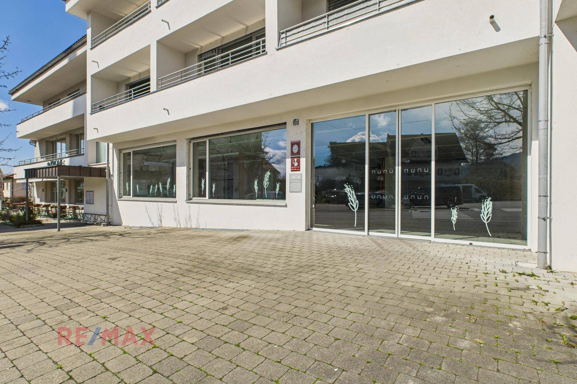 Nahaufnahme des Eingangs zum Geschäftsgebäude mit großen Glasfronten und gepflastertem Vorplatz.