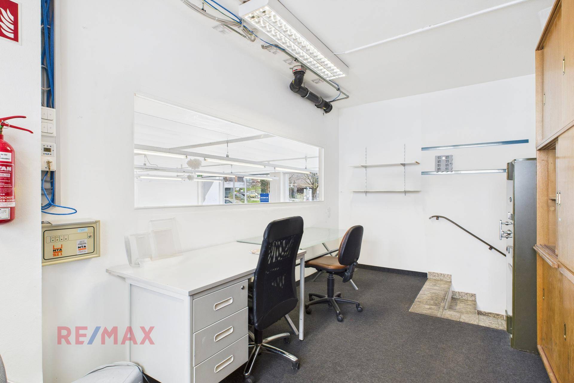 Bürobereich mit Schreibtischen, Bürostühlen und einem Fenster, das den Raum mit Licht versorgt.