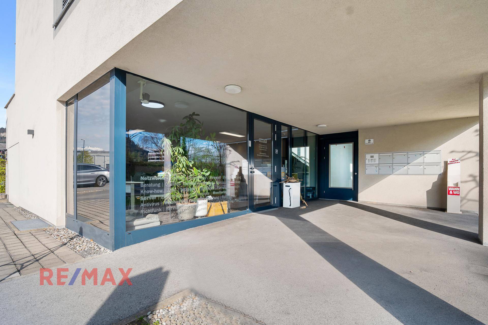 Eingangsbereich eines modernen Geschäftsgebäudes mit großen Glasfronten und überdachtem Zugang.