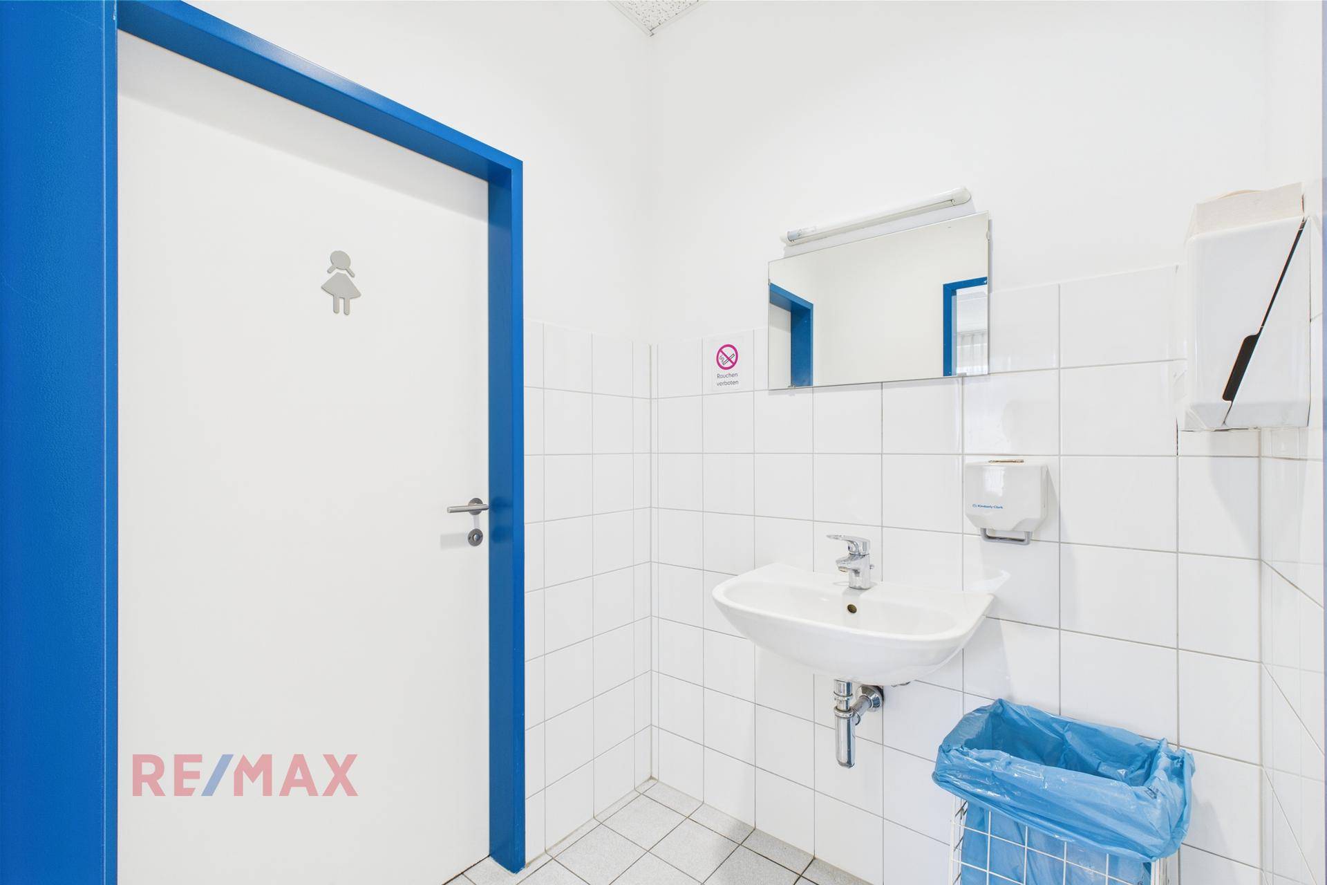 Saubere und funktionale Toilette mit weißen Fliesen, einem Waschbecken und einem Spiegel, gut gepflegt.