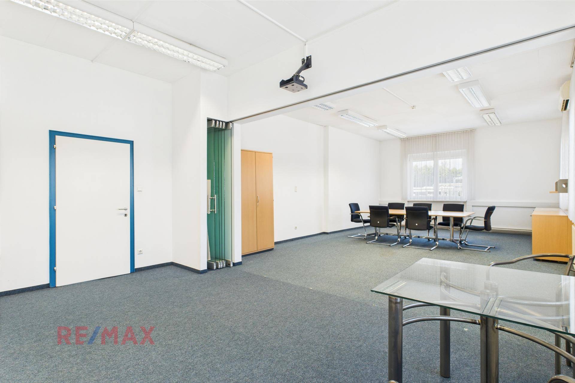 Konferenzraum mit blauem Teppichboden, Besprechungstisch und einer Glastrennwand, die flexible Raumnutzung ermöglicht.
