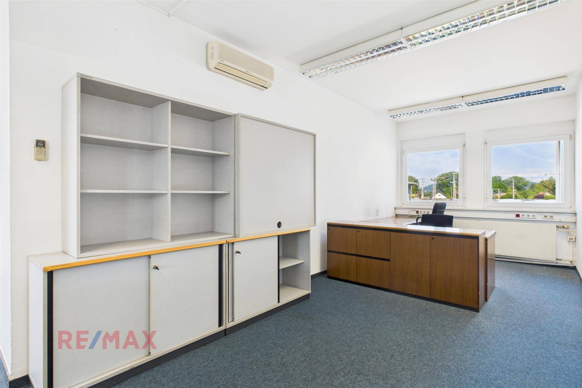 Einzelbüro mit blauem Teppichboden, großen Fenstern und Stauraum, bietet eine ruhige und produktive Arbeitsumgebung.