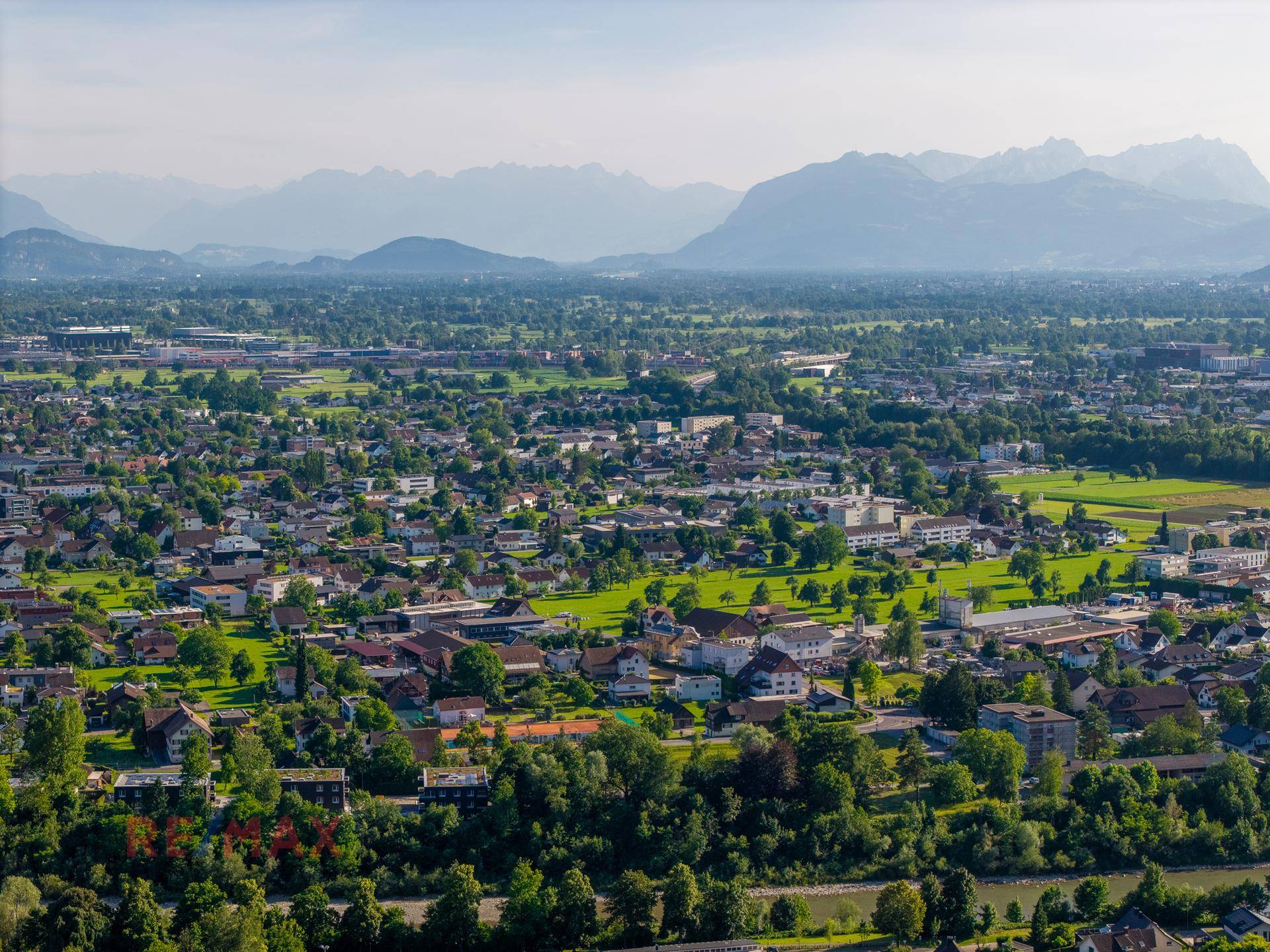 Weitläufiger Blick über die Stadtlandschaft mit grünen Hügeln und majestätischen Bergen im Hintergrund.