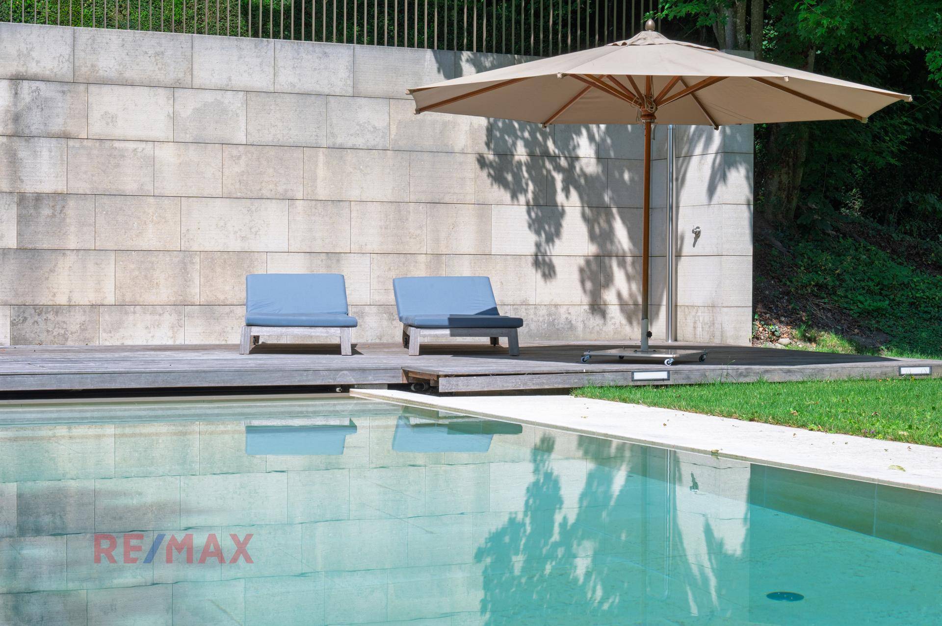 Entspannungsbereich am Pool mit Holzdeck, Liegestühlen und großem Sonnenschirm.