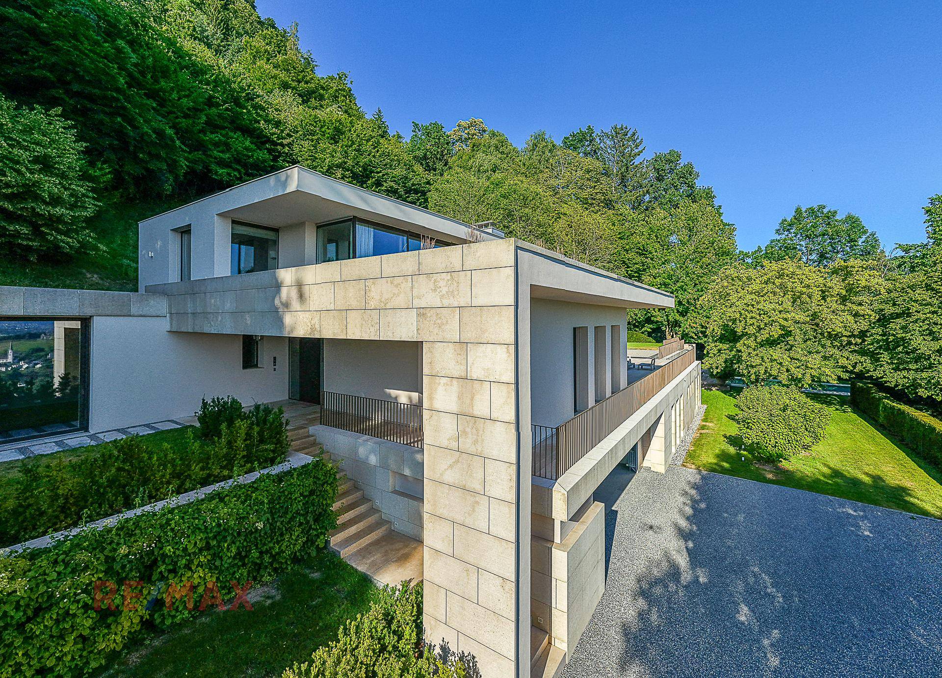 Moderne Villa mit markanter Architektur und Steinfassade, eingebettet in die bewaldete Hanglage.