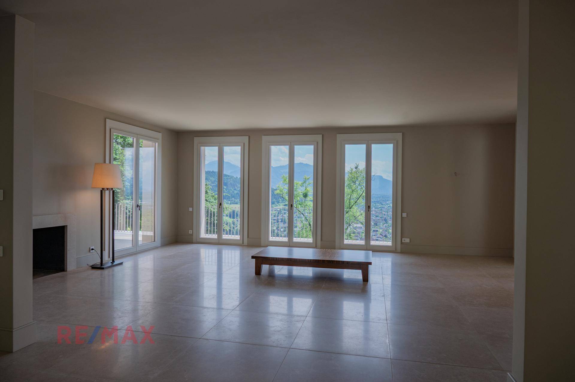 Helles Wohnzimmer mit Steinboden, Kamin und französischen Balkonen mit Bergblick.