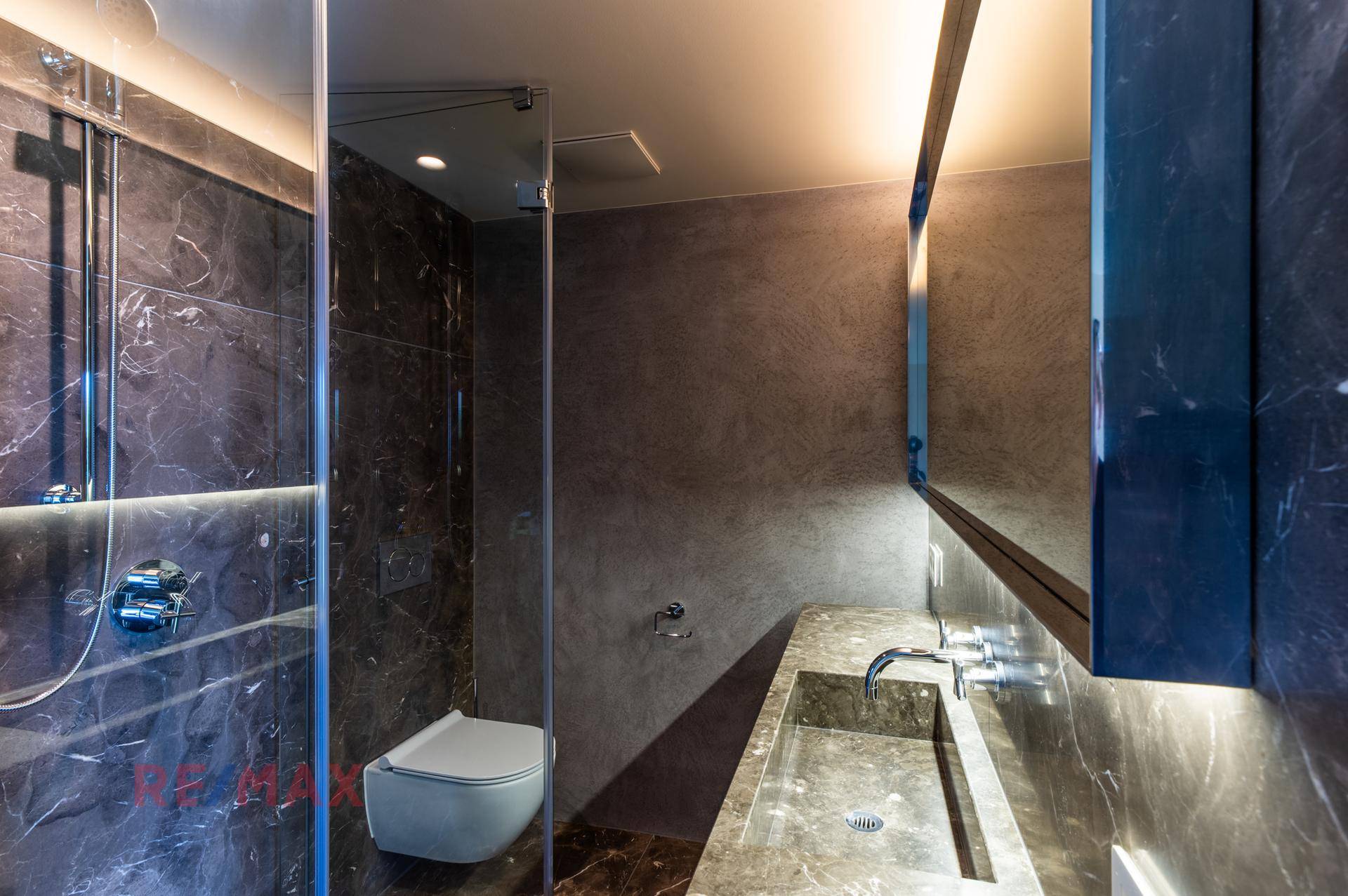 Modernes Badezimmer mit dunklen Marmorfliesen, begehbarer Dusche und elegantem Waschtisch.