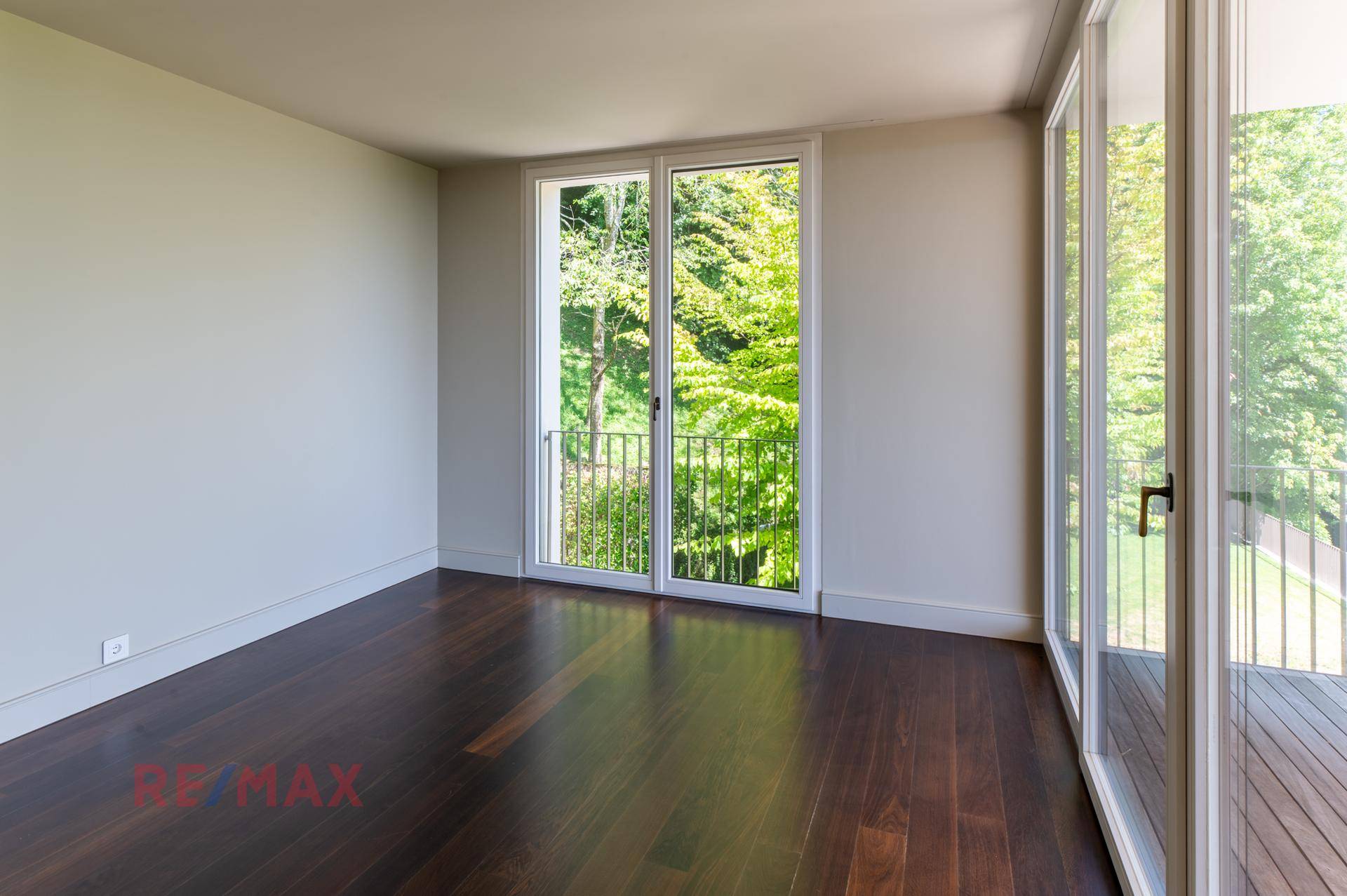 Helles Schlafzimmer mit dunklem Holzboden und Zugang zu einem französischen Balkon.