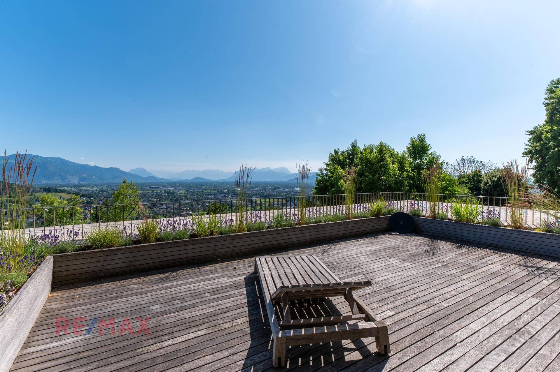 Große Holzterrasse mit Liegestuhl und weitem Blick über die Landschaft und Berge.