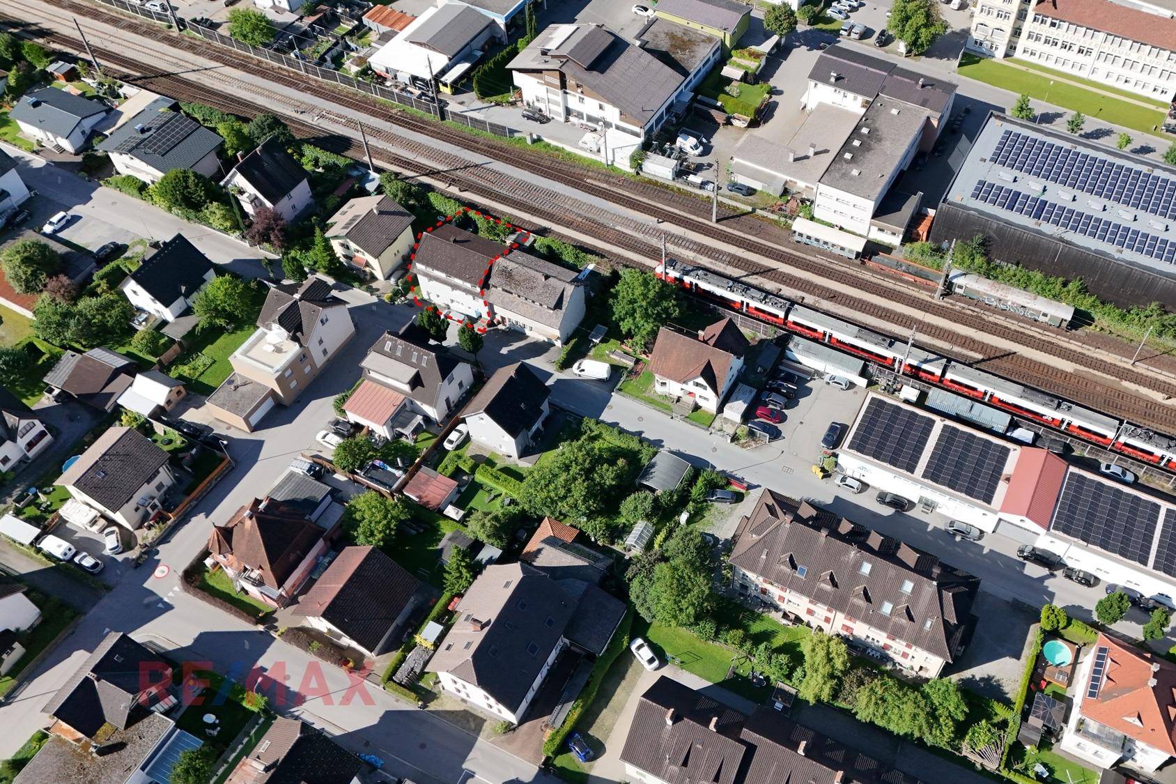 Luftaufnahme eines Wohngebiets mit Häusern, einer Bahnlinie und einem vorbeifahrenden Zug.