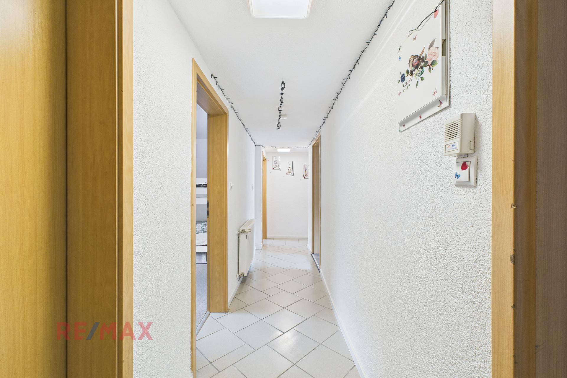 Langer, heller Flur mit weißen Wänden, Fliesenboden und mehreren Holztüren.