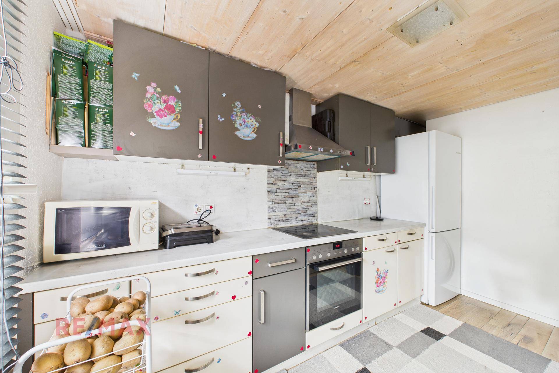 Funktionale Küche mit Holzdecke, weißen Arbeitsplatten und verschiedenen Küchengeräten.