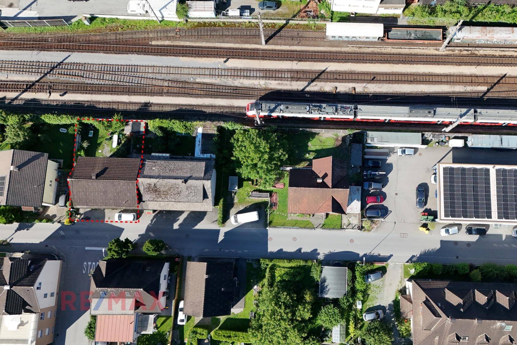 Nahaufnahme einer Luftaufnahme mit einem Wohnhaus, Bahngleisen und einem fahrenden Zug.