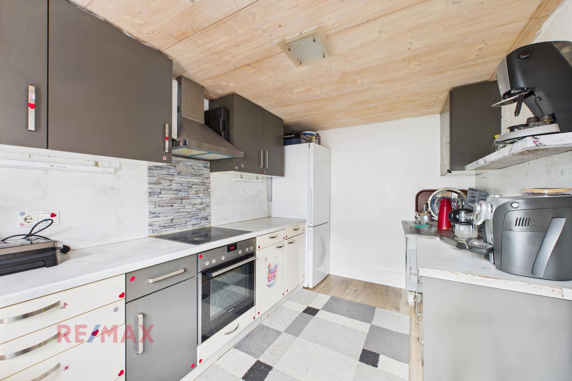 Küche mit Holzdecke, weißen Arbeitsplatten, integrierten Geräten und einer Kaffeemaschine.