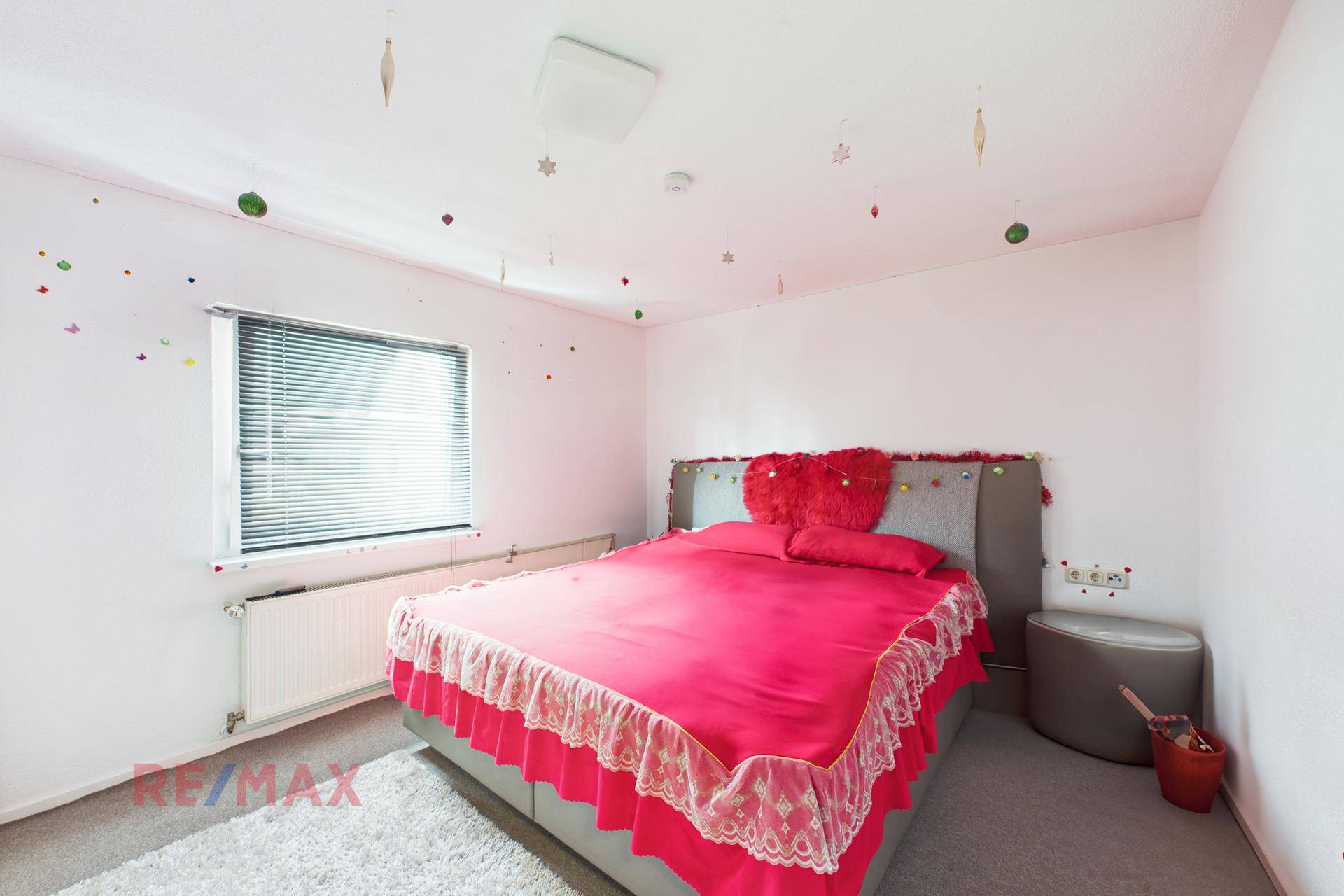 Schlafzimmer mit Doppelbett, Teppichboden und einem Fenster mit Jalousien.