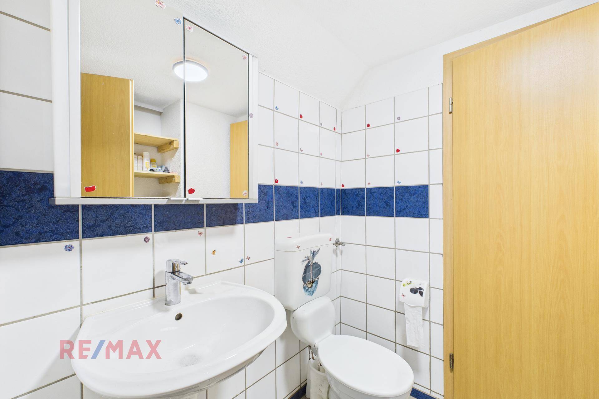 Badezimmer mit weißen und blauen Fliesen, Waschbecken, Toilette und Spiegelschrank.