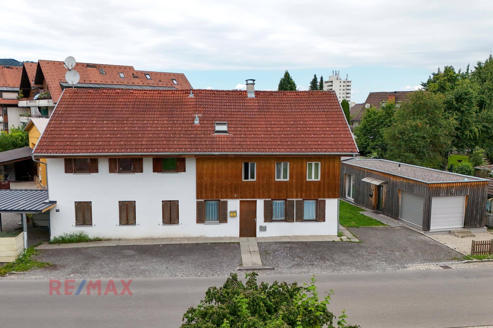 Ansicht des Wohnhauses mit weißer Fassade, Holzverkleidung und rotem Ziegeldach.