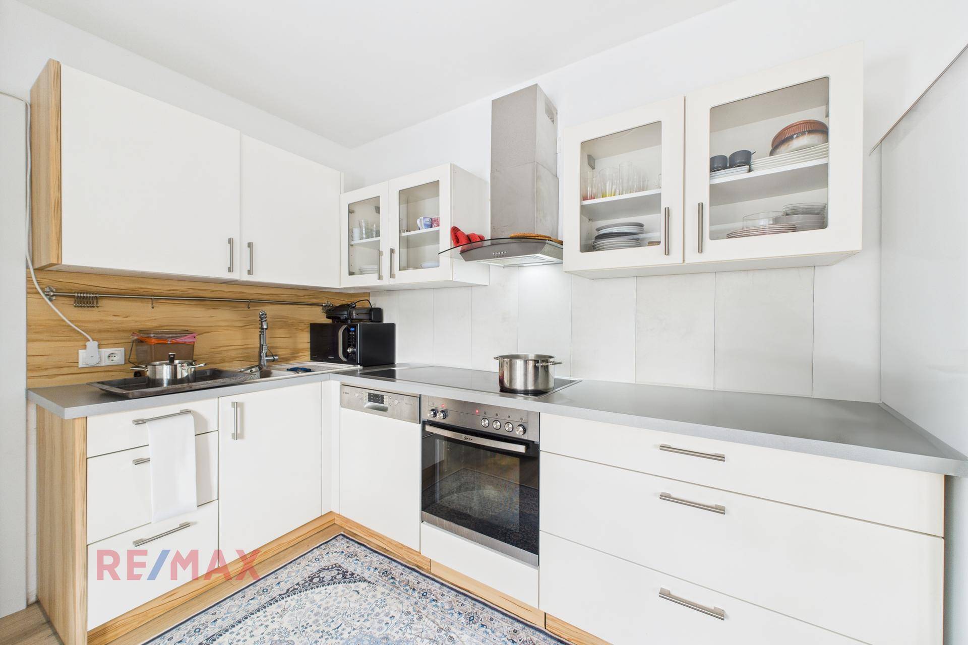 Moderne Einbauküche mit weißen Schränken, Holzdetails und Edelstahlgeräten.