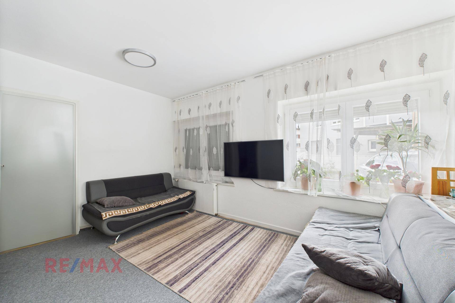 Gemütliches Wohnzimmer mit Teppichboden, Sofa und Fernseher an der Wand.