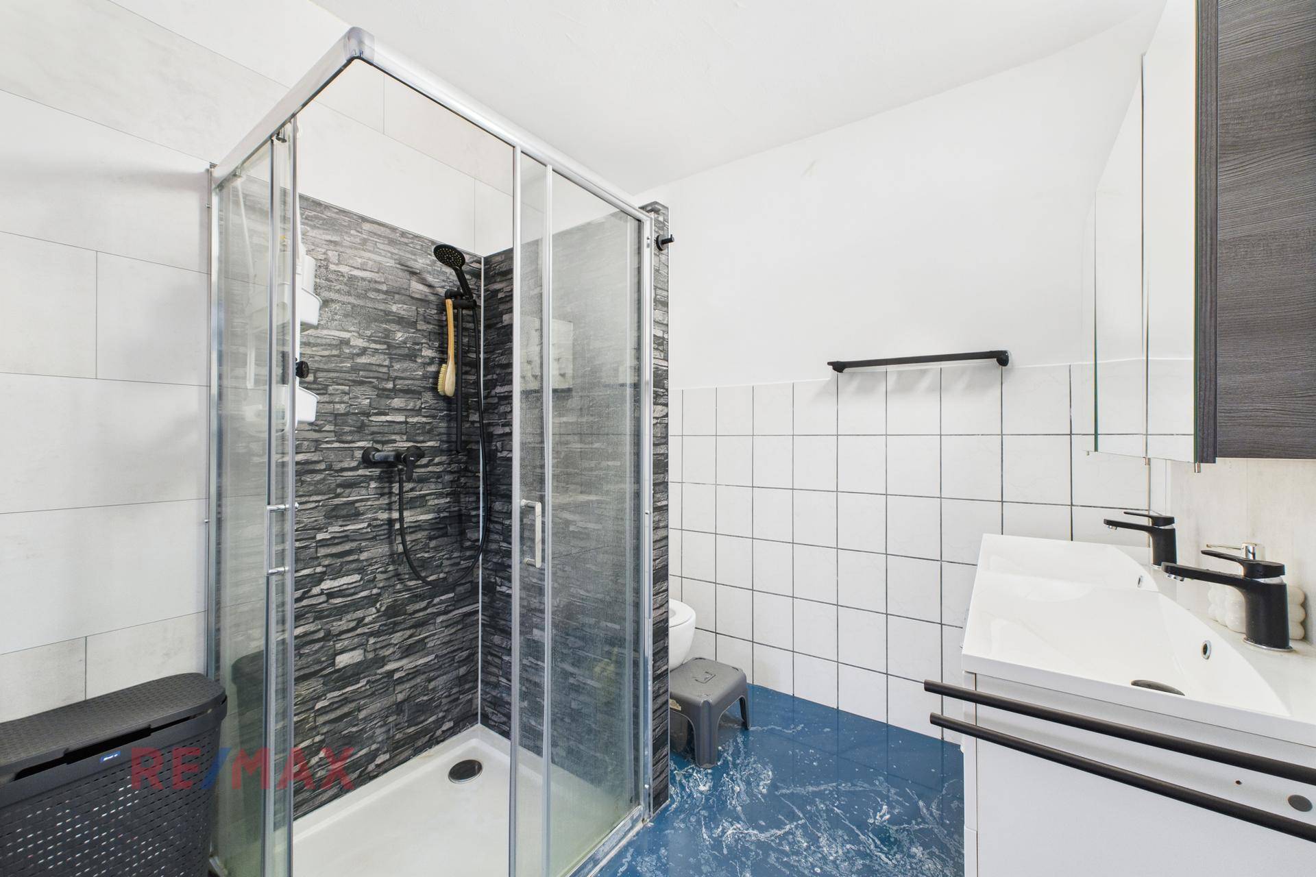 Badezimmer mit Duschkabine, modern gefliester Wand und weißem Waschbecken.