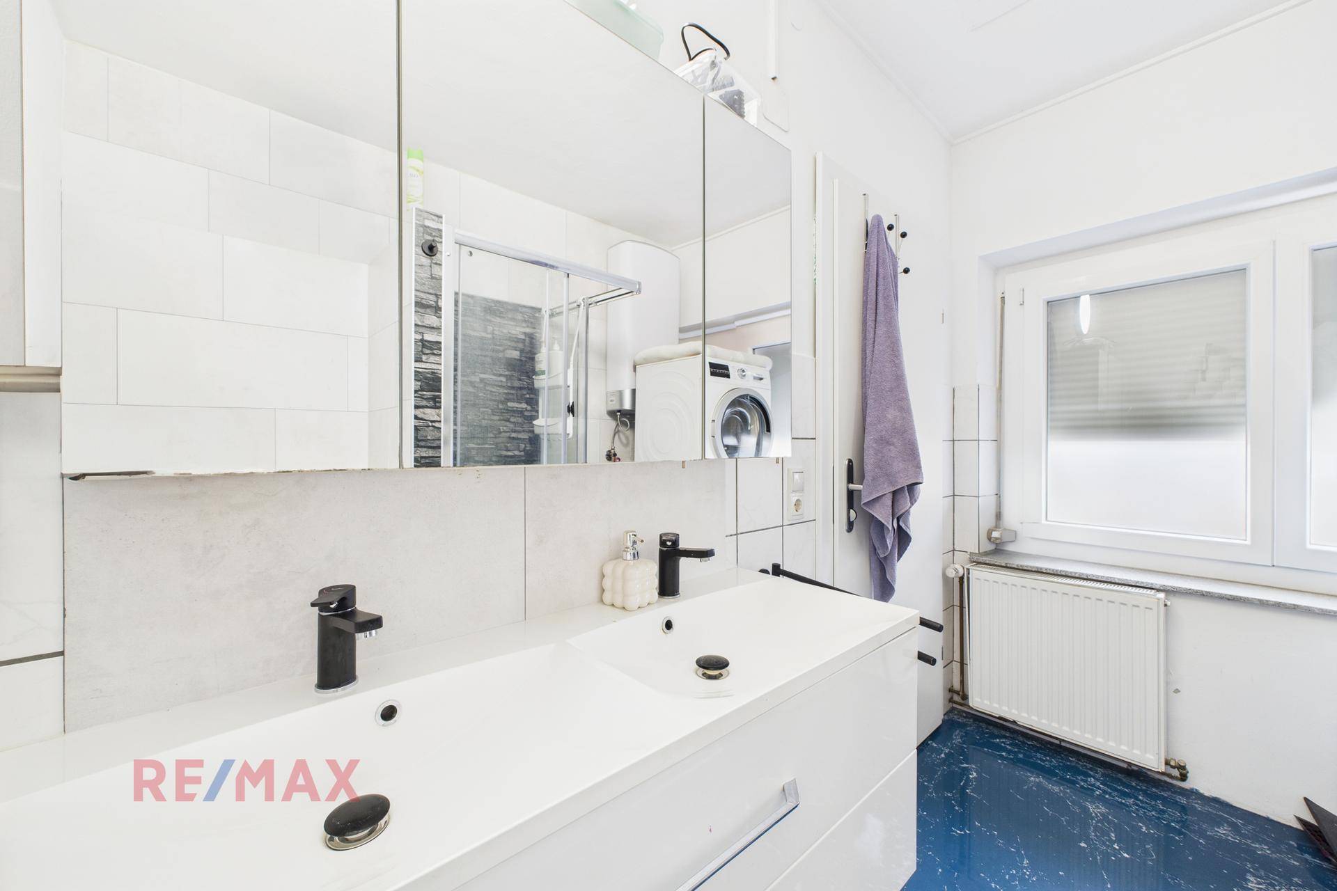 Helles Badezimmer mit Doppelwaschbecken, Spiegelschrank und Fenster für Tageslicht.
