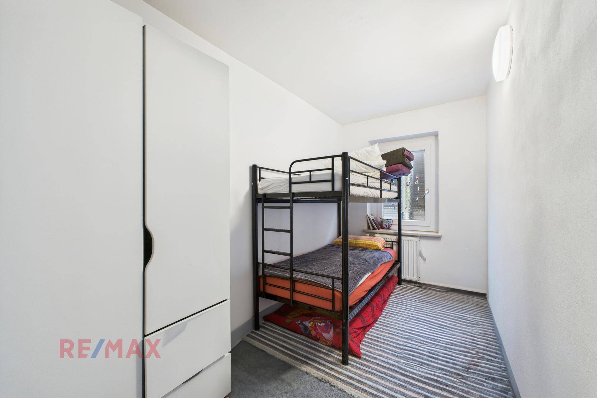 Kinderzimmer mit Etagenbett, Kleiderschrank und Fenster für natürliche Belichtung.