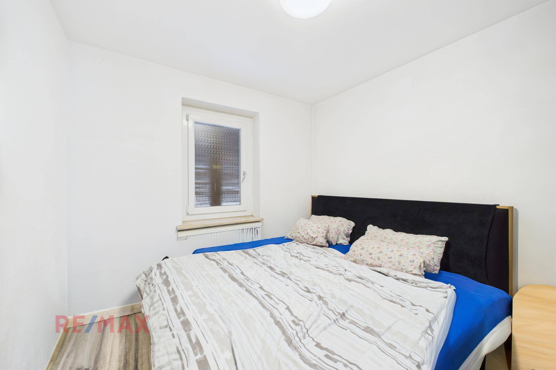 Schlafzimmer mit Doppelbett, hellem Boden und Fenster für natürliche Belichtung.