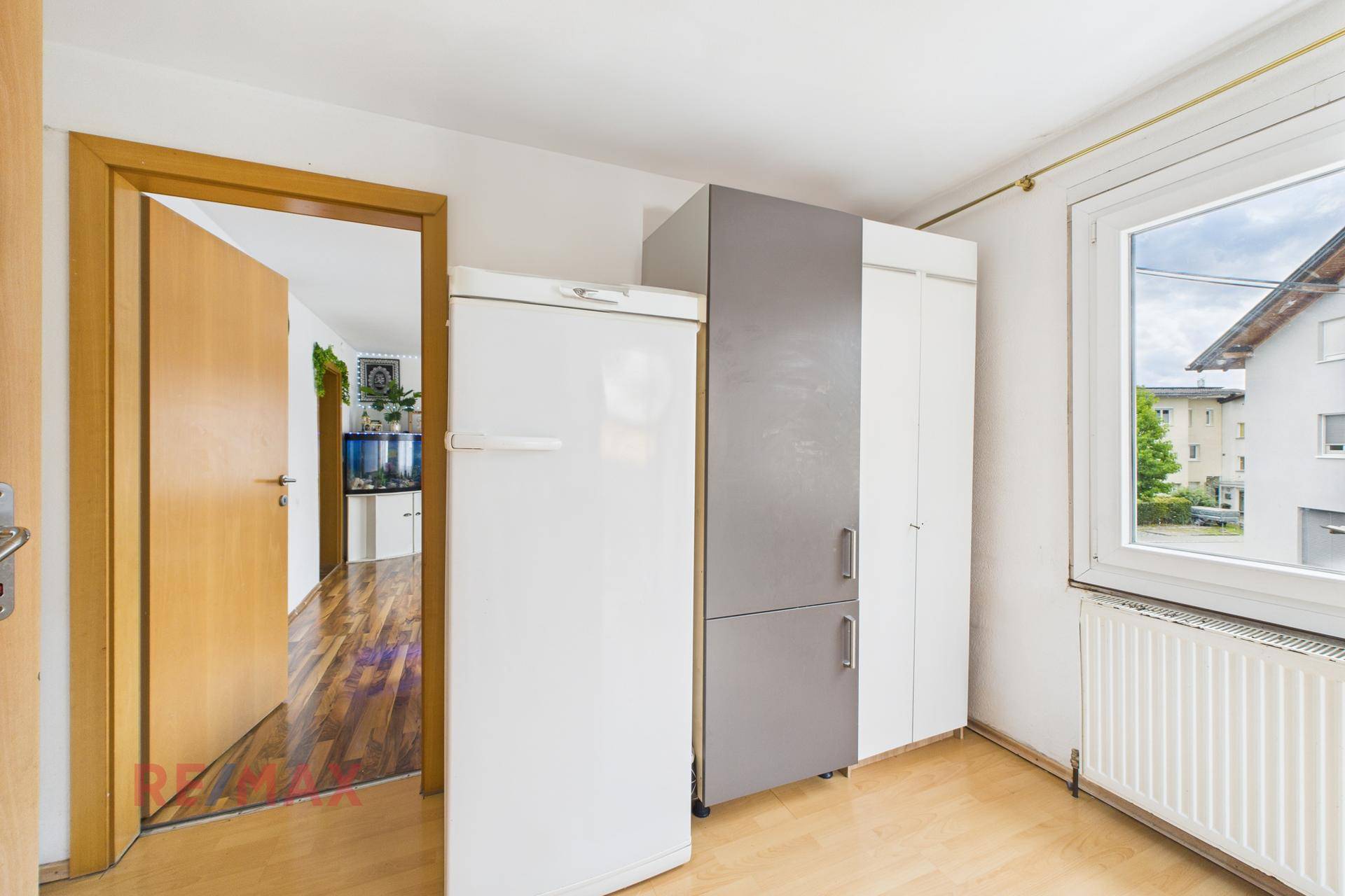 Raum mit Schränken, Kühlschrank und Fenster, möglicherweise als Abstellraum genutzt.