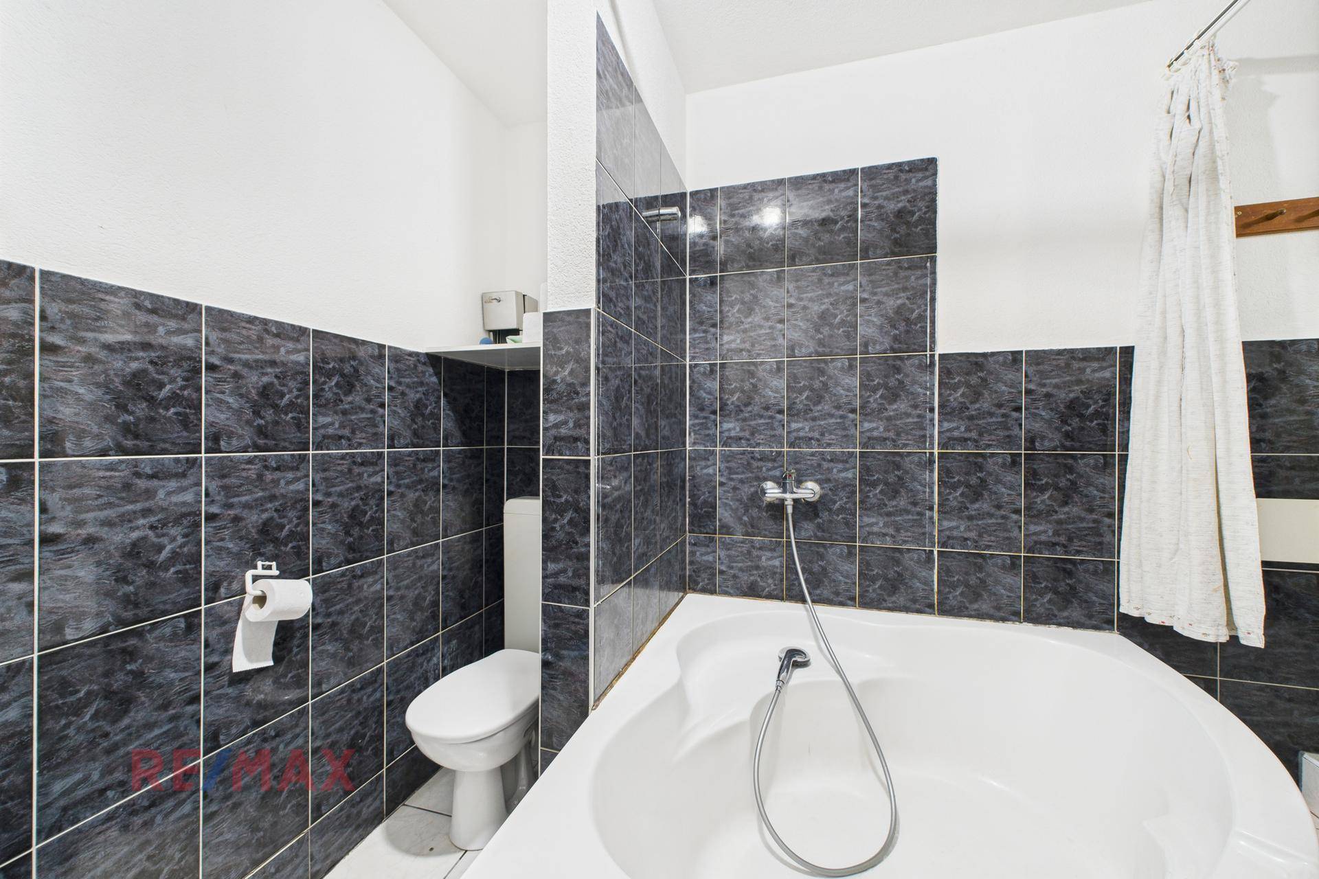 Badezimmer mit Eckbadewanne, WC und dunklen Fliesen an den Wänden.