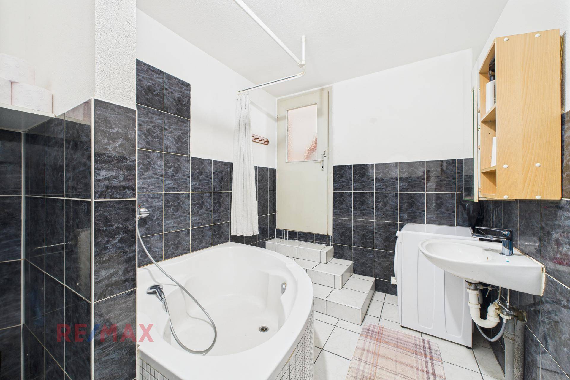 Badezimmer mit Badewanne, Waschbecken und Waschmaschine, teilweise gefliest.