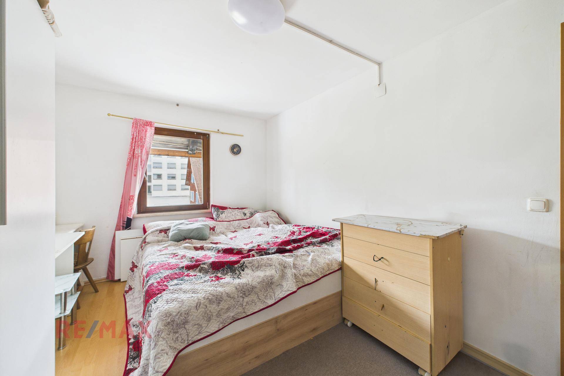 Schlafzimmer mit Doppelbett, Kommode und Fenster für natürliche Belichtung.