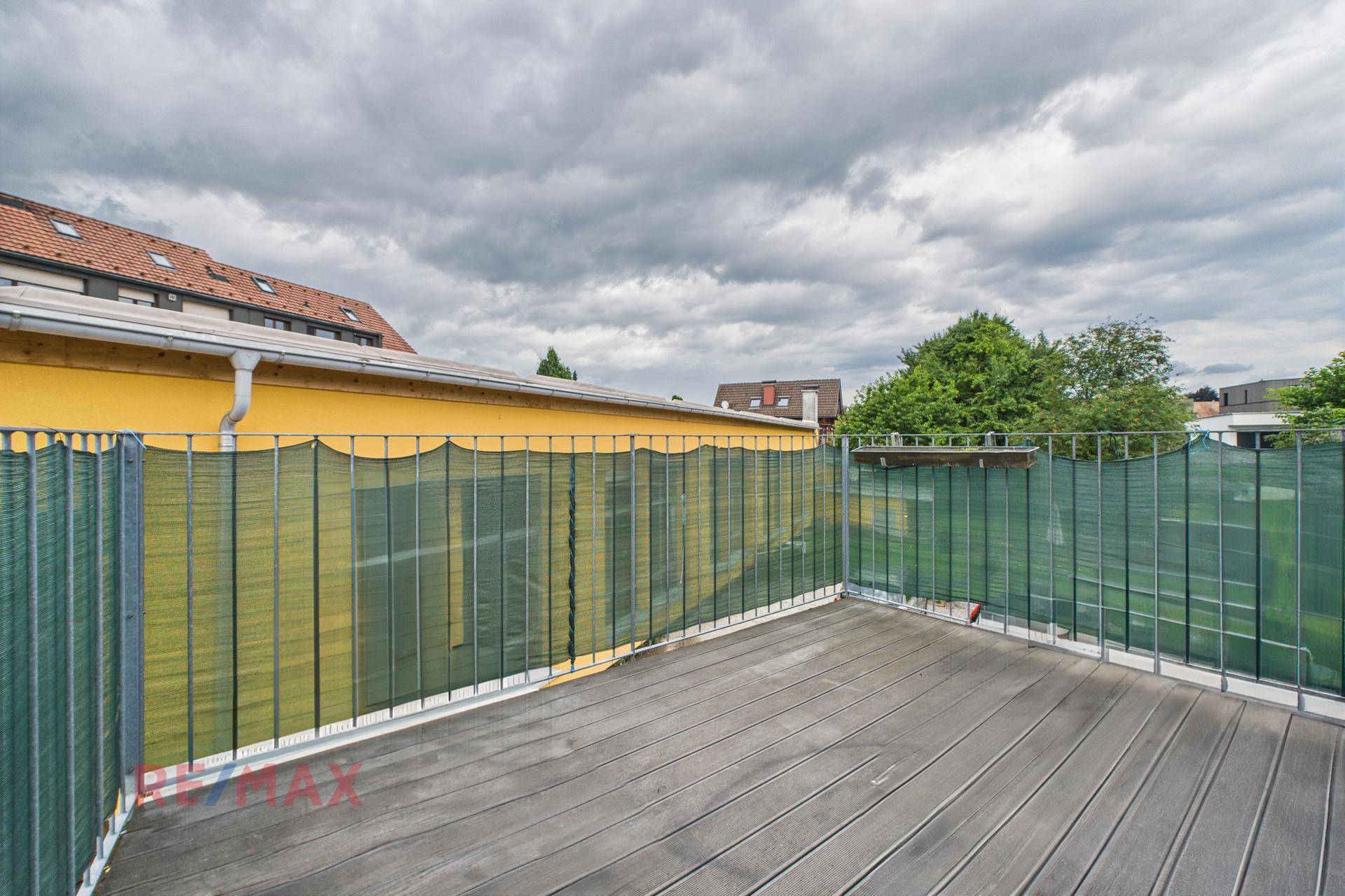 Große Holzterrasse mit Metallgeländer und Blick auf die umliegenden Gebäude.