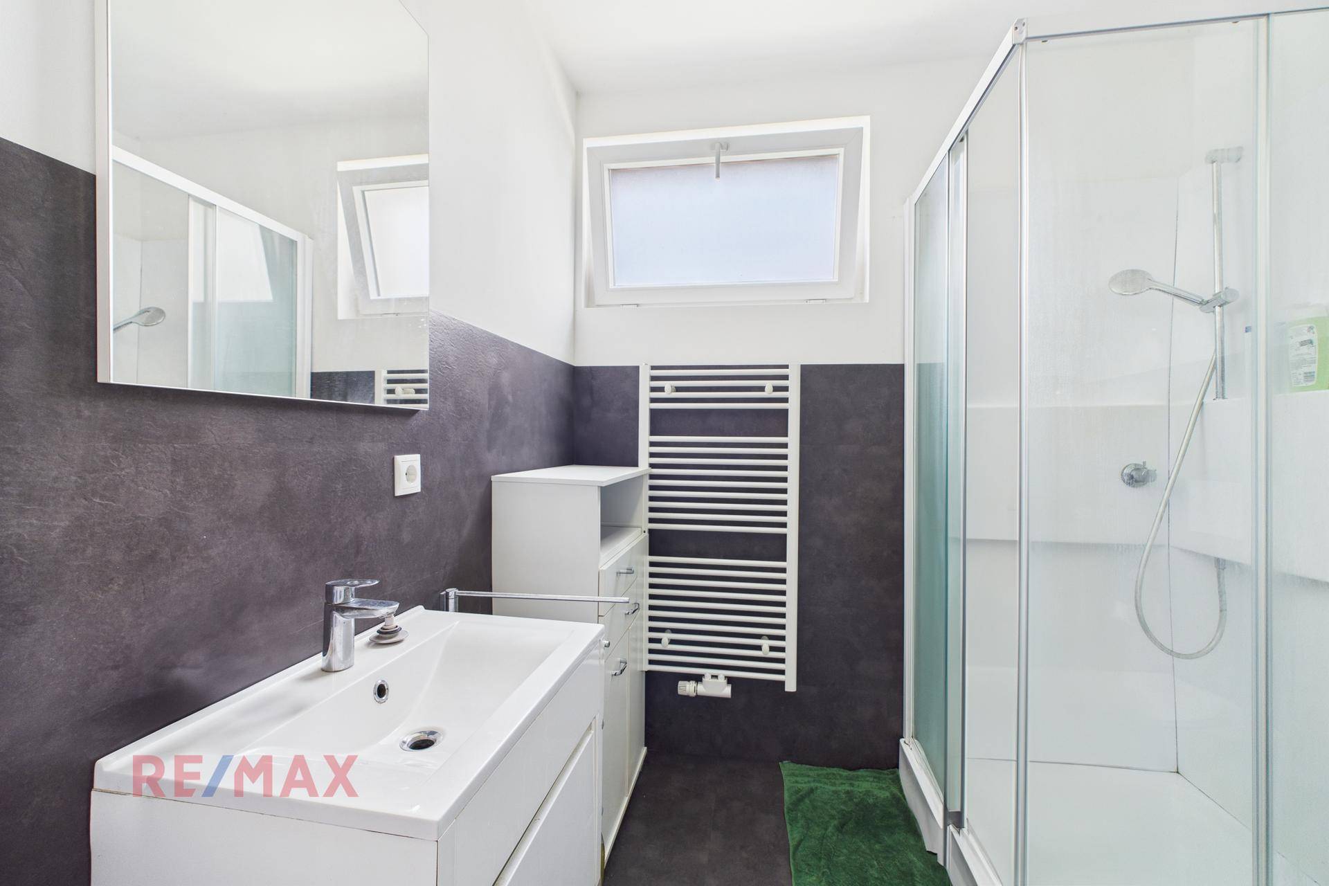 Modernes Badezimmer mit Duschkabine, Waschbecken und beheiztem Handtuchhalter.