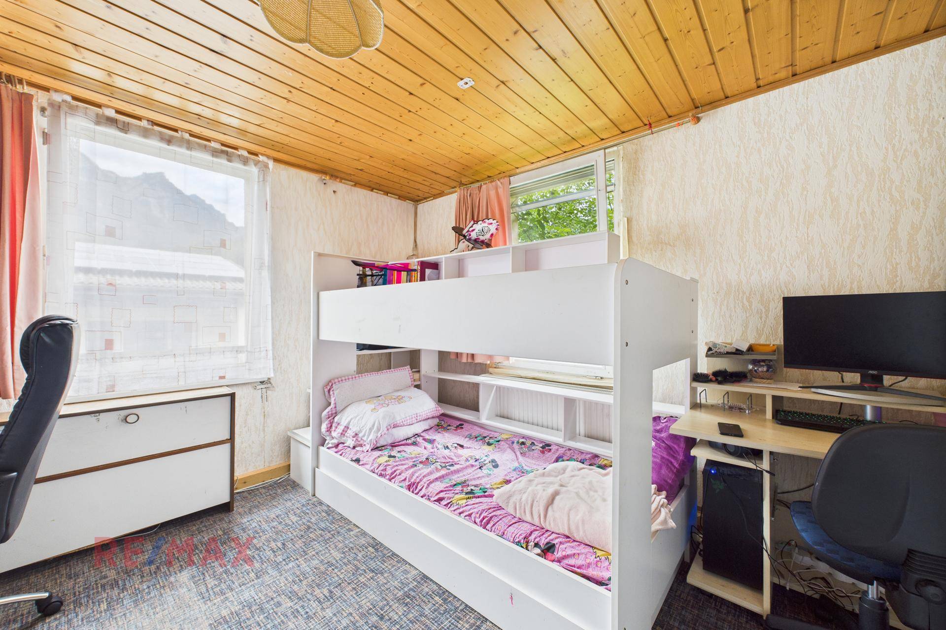 Helles Kinderzimmer mit Etagenbett, Schreibtisch und Holzdecke, hell durch großes Fenster.