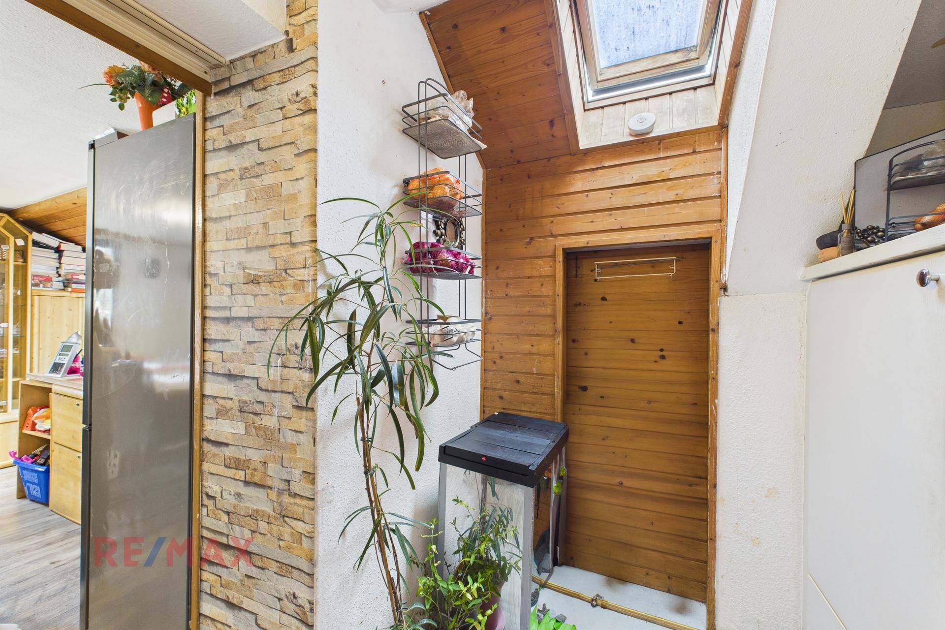 Heller Flur mit Holzverkleidung, dekorativer Pflanze und natürlichem Licht durch Dachfenster.